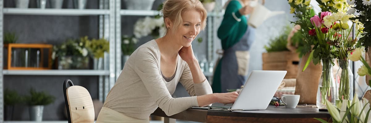 Vrouw zit aan tafel met erop een vaas met bloemen en kijkt blij naar haar laptop om scan en herken software te vergelijken.