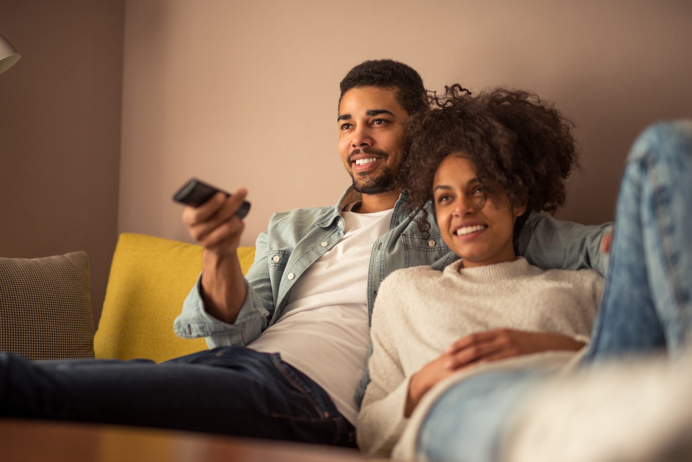 Hombre y mujer ven la tele en el sofá con el mando a distancia en la mano