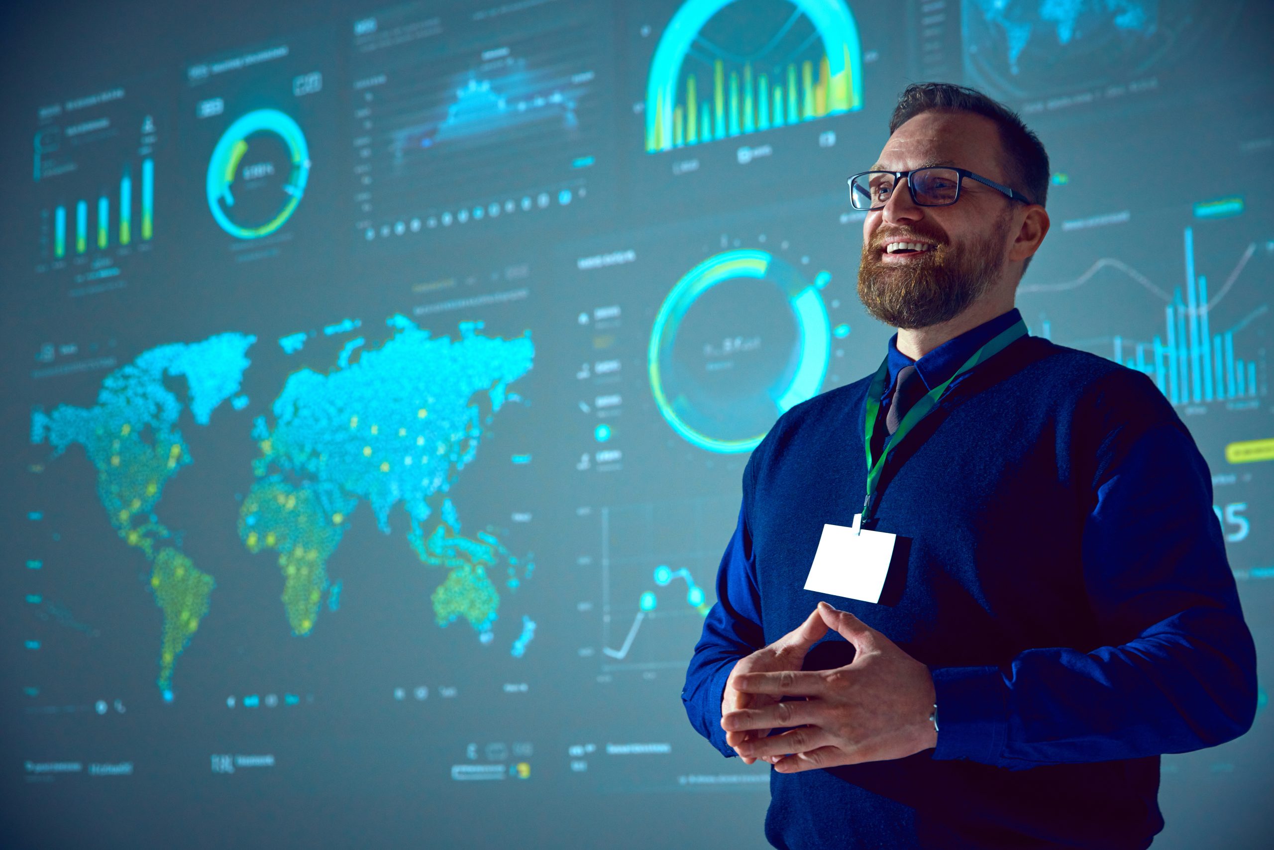 Lachende zakenman met een bril die analytische datavisualisaties op groot scherm presenteert en lijkt te werken met PowerBI.