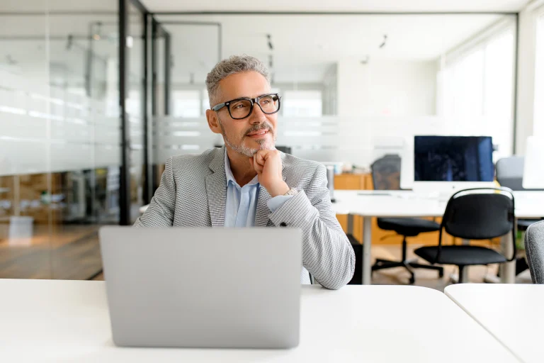 Man die achter een computer zit, kijkt nadenkend uit het raam alsof hij nieuwe inzichten opdoet naar aanleiding van data analytics