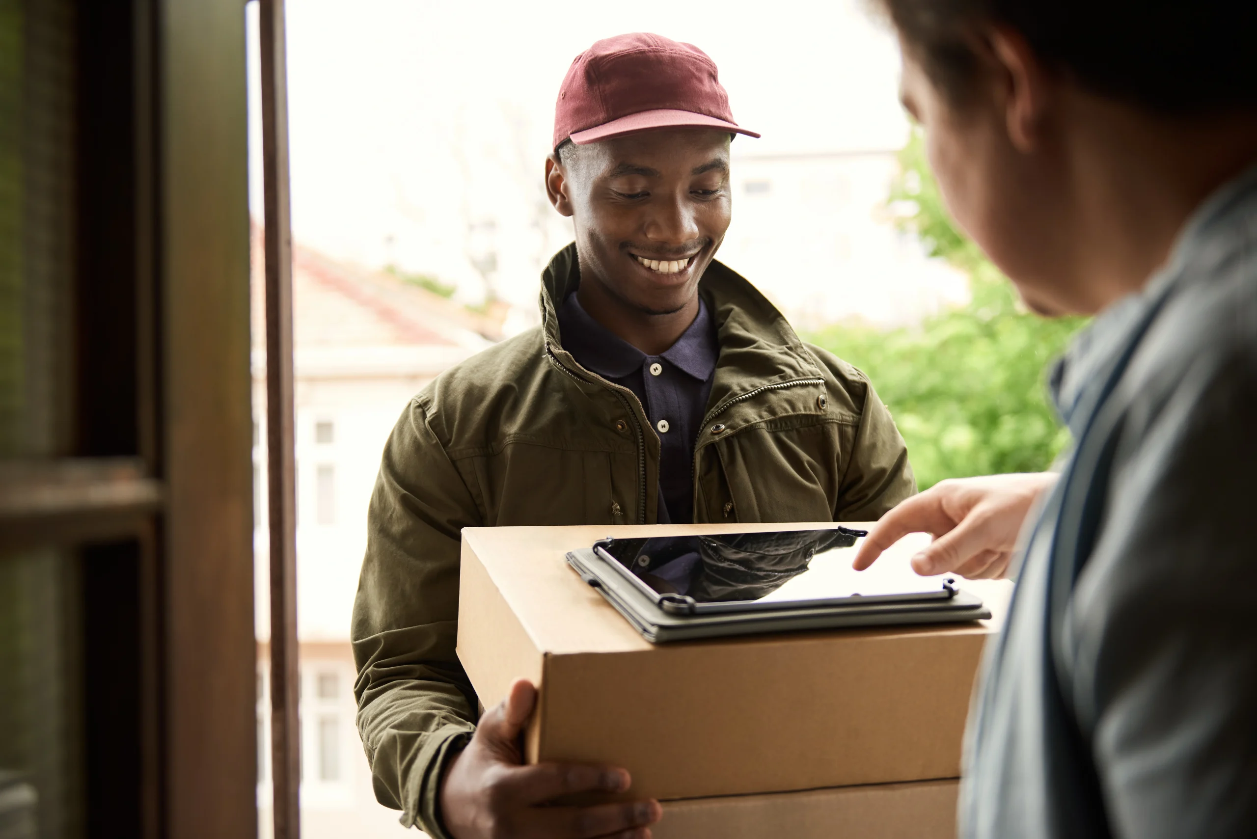 Man laughingly offers a parcel while the recipient is busy digitally signing a pdf.