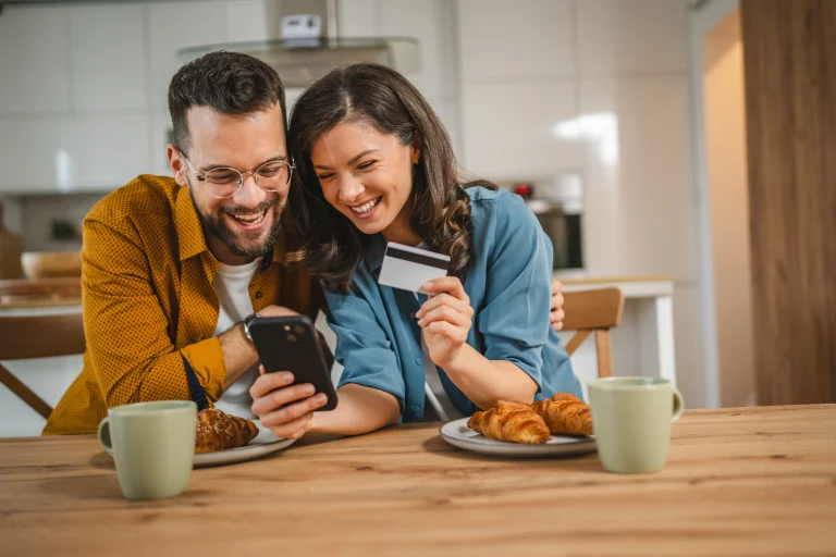 Een man en een vrouw zitten lachend tegen elkaar aan te kijken naar een telefoon, terwijl ze een bankrekening openen.