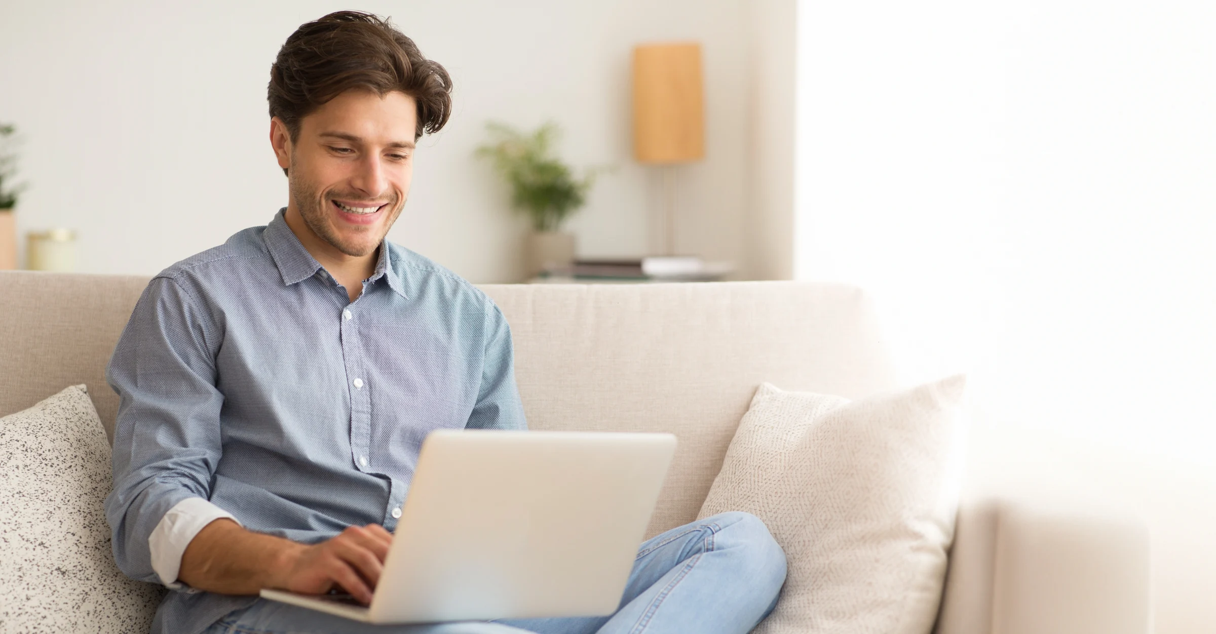 A man sits smiling on a sofa, holding a laptop on his lap, communicating with a creditor.