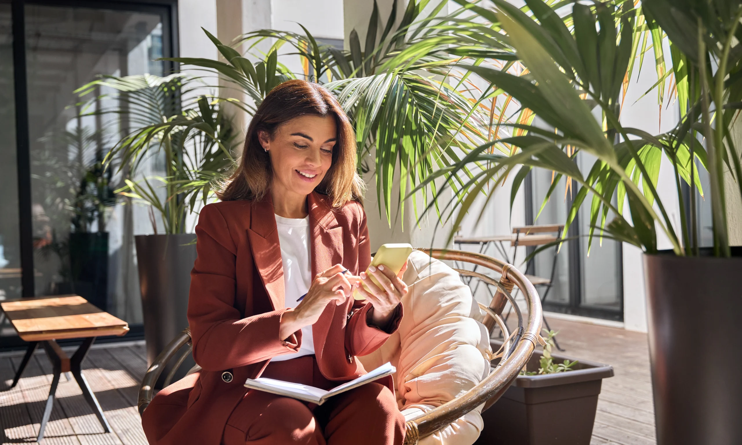 Une femme est assise sur une chaise dans le jardin d'hiver et travaille avec une application de chèques sur son téléphone.