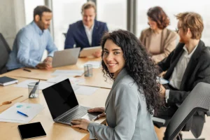 Een vrouw kijkt lachend in de camera terwijl ze werkt op een laptop met een ERP-systeem.