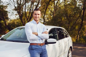 Een man leunt op een auto en kijkt in de camera, vlak voordat hij op het punt staat naar een debiteur te rijden.