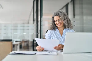 Een vrouw zit lachend achter een laptop om factuurgegevens te verwerken.