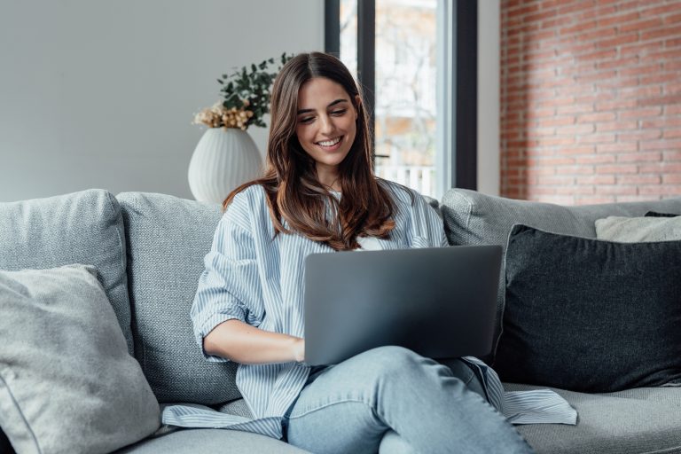 Een vrouw werkt lachend op haar computer, terwijl ze kostenplaatsen verwerkt.